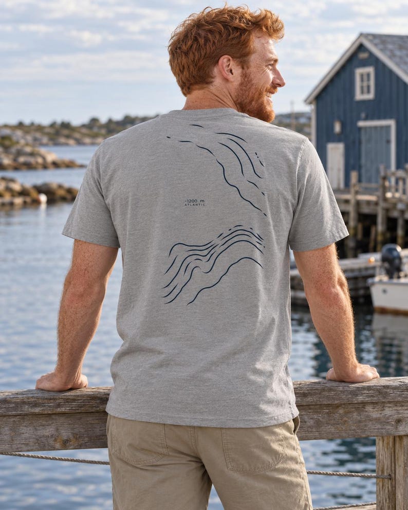K&ouml;nnte beinhalten: Ein graumeliertes Kurzarm-T-Shirt mit einer dunkelblauen Linien-Grafik auf der R&uuml;ckseite. Das Design zeigt topografische H&ouml;henlinien und enth&auml;lt den Text -1200 m ATLANTIC, der in einer kleinen, klaren Schrift zwischen den Linien gedruckt ist.