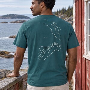 K&ouml;nnte beinhalten: Ein dunkelblaugr&uuml;nes Kurzarm-T-Shirt mit einer wei&szlig;en Liniengrafik auf der R&uuml;ckseite, die topografische Tiefenlinien des Ozeans darstellt. Der Text "-1200 m" und "ATLANTIC" steht in kleinen wei&szlig;en Buchstaben zwischen den wellenf&ouml;rmigen Linien.