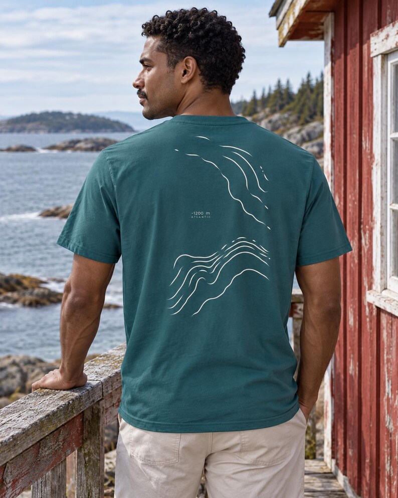 K&ouml;nnte beinhalten: Ein dunkelblaugr&uuml;nes Kurzarm-T-Shirt mit einer wei&szlig;en Liniengrafik auf der R&uuml;ckseite, die topografische Tiefenlinien des Ozeans darstellt. Der Text "-1200 m" und "ATLANTIC" steht in kleinen wei&szlig;en Buchstaben zwischen den wellenf&ouml;rmigen Linien.