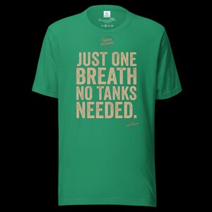 May include: A bright green short-sleeve t-shirt featuring the beige text "JUST ONE BREATH NO TANKS NEEDED." printed on the front. The shirt includes a small circular logo above the text and a smaller circular graphic near the bottom right corner.