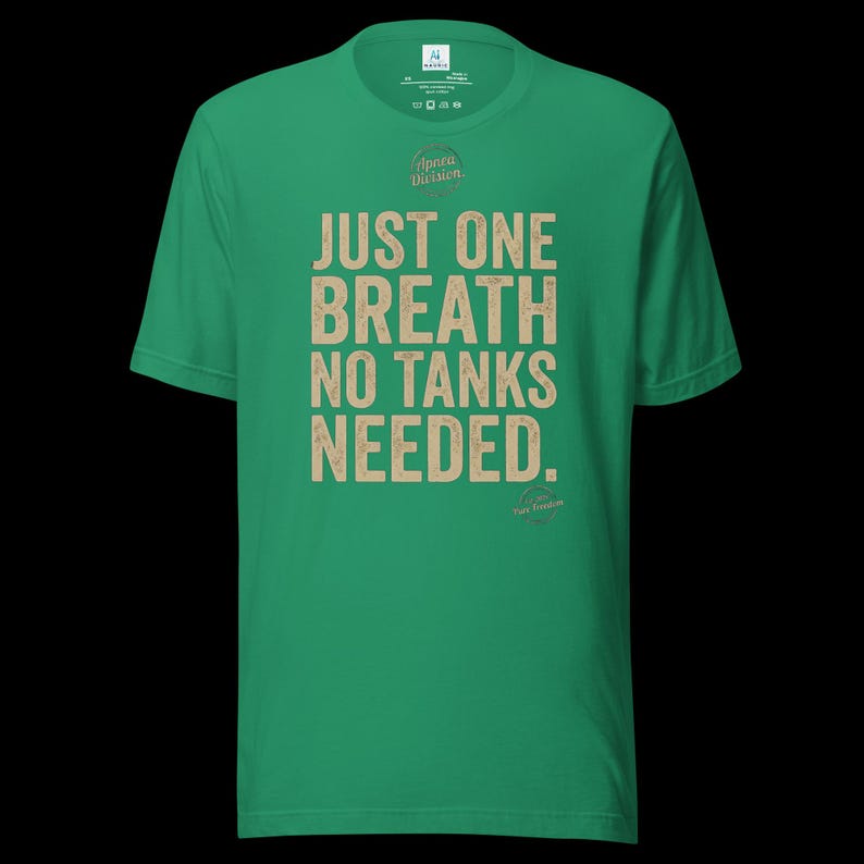 May include: A bright green short-sleeve t-shirt featuring the beige text "JUST ONE BREATH NO TANKS NEEDED." printed on the front. The shirt includes a small circular logo above the text and a smaller circular graphic near the bottom right corner.