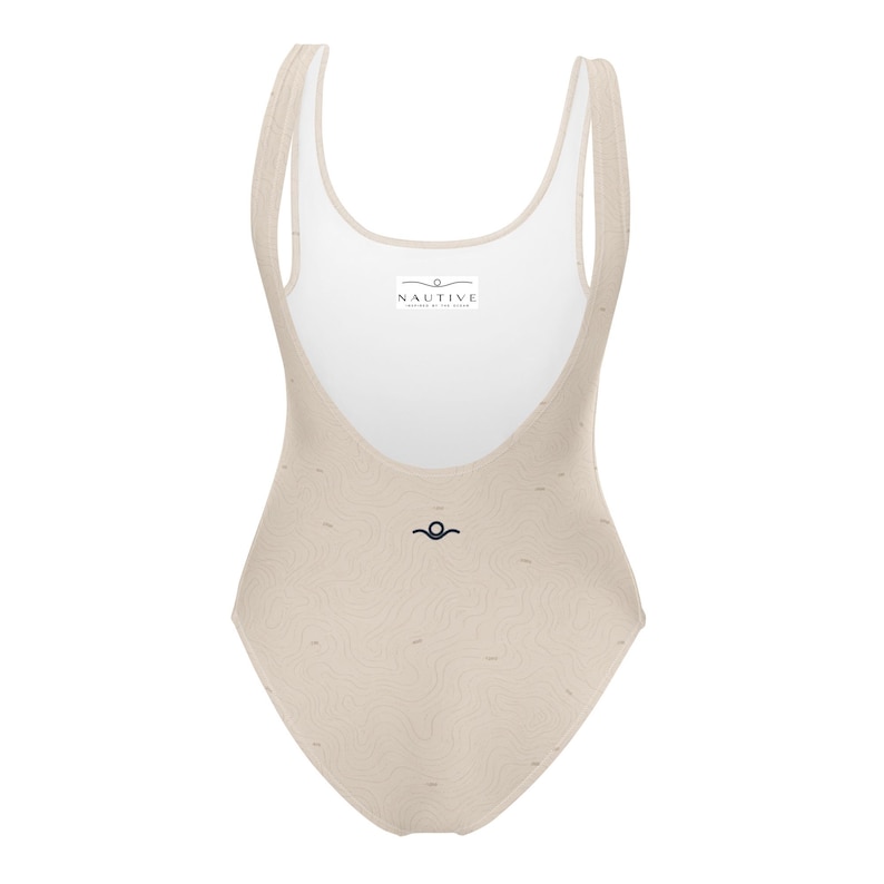 Peut inclure: Un maillot de bain une pi&egrave;ce beige avec un motif subtil de lignes ondul&eacute;es. Le v&ecirc;tement pr&eacute;sente une encolure d&eacute;gag&eacute;e et une doublure int&eacute;rieure blanche avec une &eacute;tiquette rectangulaire portant l'inscription NAUTIVE. Un petit logo noir est centr&eacute;.