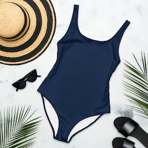 Peut inclure: Un maillot de bain une pi&egrave;ce bleu marine orn&eacute; d'un motif topographique ton sur ton discret. Le v&ecirc;tement pr&eacute;sente une encolure d&eacute;gag&eacute;e et de larges bretelles. Il est pr&eacute;sent&eacute; avec un chapeau de paille, des lunettes noires et des sandales.