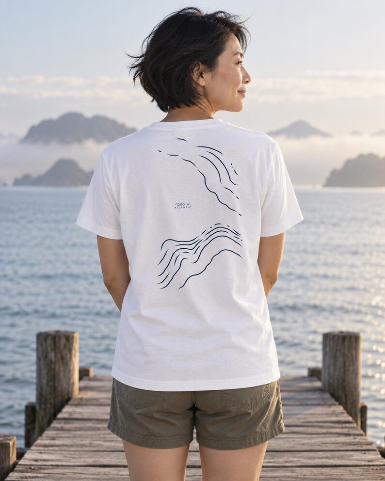 K&ouml;nnte beinhalten: Ein wei&szlig;es Kurzarm-T-Shirt mit einem dunkelblauen Grafikdruck auf der R&uuml;ckseite. Das Design besteht aus zwei S&auml;tzen wellenf&ouml;rmiger Linien, die die Ozeantopografie darstellen, mit dem Text -1200 m ATLANTIC in der Mitte dazwischen.