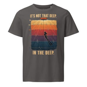 May include: A charcoal gray t-shirt featuring a graphic of a diver underwater with a heart rate monitor line. The text reads IT'S NOT THAT DEEP. IN THE DEEP. The design includes depth markers from 0m to 50m in a colorful, layered background.