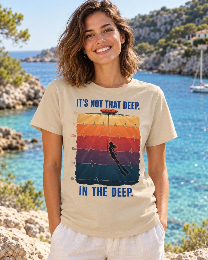 May include: A beige short-sleeve t-shirt featuring a graphic of a freediver descending through colorful water layers with depth markers from 0m to 50m, an EKG heartbeat line, and the text IT'S NOT THAT DEEP. IN THE DEEP. printed in blue.