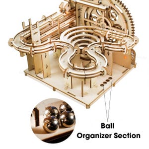 May include: A wooden marble run kit with a complex track design, featuring multiple loops, gears, and a ball organizer section. The kit is made of light-colored wood and includes several metal marbles.