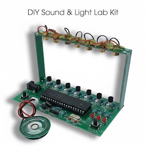 May include: DIY Sound & Light Lab Kit. A green circuit board with various electronic components, including a speaker, resistors, and a microchip. The kit includes a frame with lights and wires, and the text "DIY Sound & Light Lab Kit" is at the top.