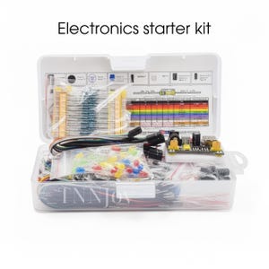 Könnte beinhalten: Geöffnete weiße Kunststoff-Elektronik-Starter-Kit, gefüllt mit verschiedenen Komponenten wie Widerständen, LEDs und Drähten. Das Kit enthält eine gedruckte Anleitung und ist mit "Electronics starter kit" beschriftet. Das Kit ist für Bildungszwecke konzipiert.