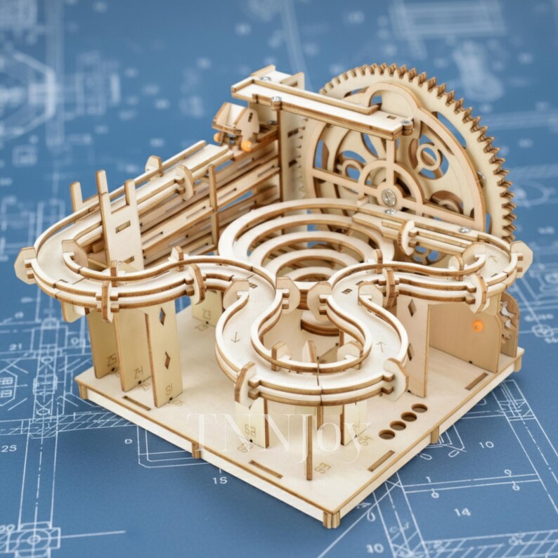 May include: A wooden marble run kit, featuring a complex track design with loops, gears, and ramps. The natural wood color contrasts against a blue background with a blueprint design. The kit is designed for assembly and play.