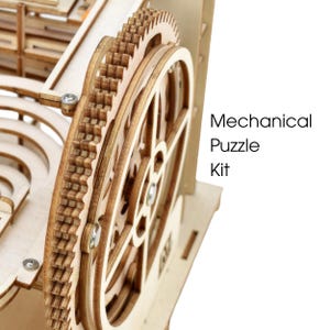 May include: Close-up of a wooden mechanical puzzle kit. The image shows intricate gears and a wheel, all made of light-colored wood. The text "Mechanical Puzzle Kit" is visible on the right side of the image.