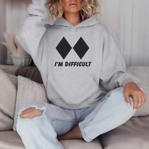 May include: A grey hooded sweatshirt with black diamond symbols and the text "I'M DIFFICULT" printed on the front.