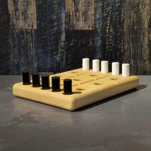 Könnte beinhalten: Ein Holzbrettspiel mit hellem Holzfinish. Das Spielbrett hat ein Raster von Löchern und enthält schwarze und weiße zylindrische Spielsteine. Das Spiel ist vor einem dunklen Holzhintergrund aufgebaut.