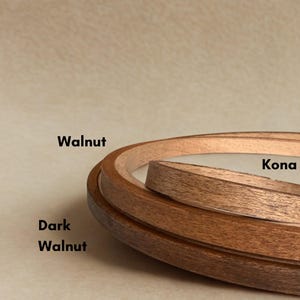 May include: Three wooden embroidery hoops in shades of brown: Walnut, Kona, and Dark Walnut. The hoops are nested, displaying the different wood tones and textures. Text labels indicate each hoop's colour.