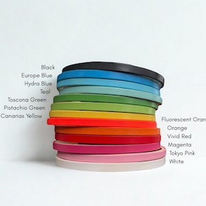 Pode incluir: Uma pilha de bastidores de bordado circulares em várias cores, incluindo preto, azul Europa, azul Hydra, azul-petróleo, verde Toscana, verde pistache, amarelo Canárias, laranja fluorescente, laranja, vermelho vivo, magenta, rosa Tokyo e branco, com etiquetas.