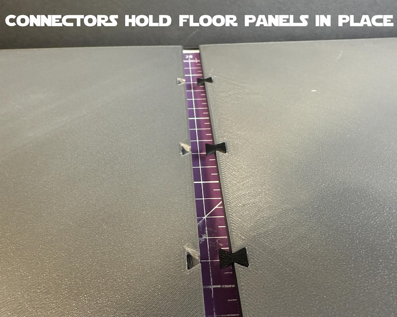 Puede incluir: Primer plano de dos paneles de suelo grises con una regla morada en el medio. Se ven conectores negros que sujetan los paneles. El texto "CONNECTORS HOLD FLOOR PANELS IN PLACE" est&aacute; en la parte superior.