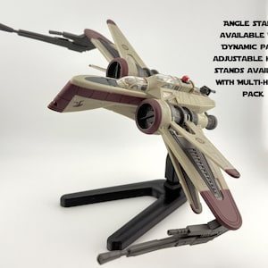 Könnte beinhalten: Ein cremefarbenes und burgunderfarbenes Modell eines Raumjägers, montiert auf einem schwarzen Ständer. Das Modell hat detaillierte Flügel und Triebwerke. Text: ANGLE STANDS AVAILABLE WITH DYNAMIC PACK. ADJUSTABLE HEIGHT STANDS AVAILABLE WITH MULTI-HEIGHT PACK.