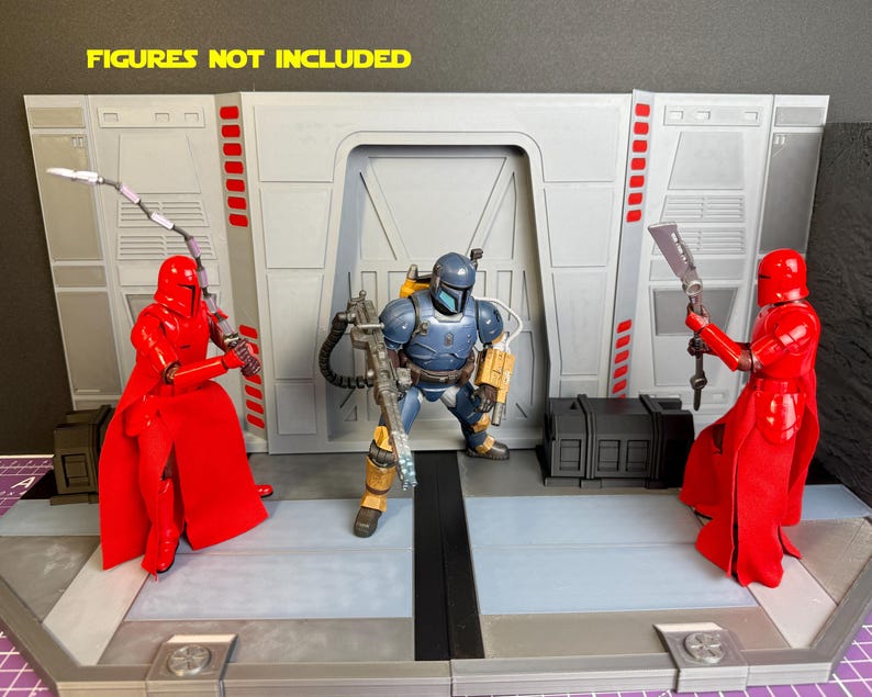 Puede incluir: Un diorama tem&aacute;tico de Star Wars con un interior gris y blanco y una puerta central. Dos figuras rojas con armas flanquean una figura blindada azul y amarilla. El texto "FIGURES NOT INCLUDED" se muestra en la parte superior.