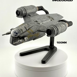 Pode incluir: Modelo detalhado de uma nave espacial cinza com detalhes amarelos, exibido em um suporte preto e uma base circular branca. O texto "SHIP NOT INCLUDED" é visível. O modelo tem aproximadamente 10 cm de comprimento.