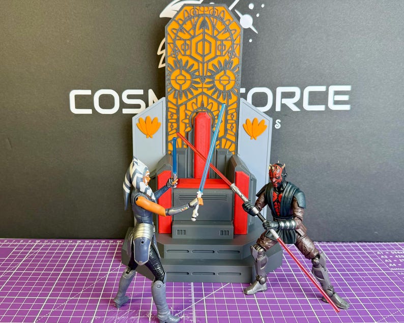 May include: Action figures of Ahsoka Tano and Darth Maul engaged in a lightsaber duel in front of a throne. The throne is gray, orange, and gold. The background has the text "COSMOS FORCE". The figures are on a purple grid.