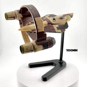以下が含まれることがあります： 茶色とベージュの色合いの宇宙船モデルで、黒いスタンドに取り付けられています。 宇宙船はユニークな翼のデザインで、長さは約10cmです。「SHIP NOT INCLUDED」と「100MM」の文字が見えます。