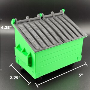 May include: A green plastic toy dumpster with a grey lid. The dumpster is 5 inches long, 4.25 inches tall, and 2.75 inches wide.