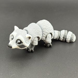 May include: A grey and white articulated raccoon toy with black eyes and a black nose. The toy is made of plastic and has a segmented tail.