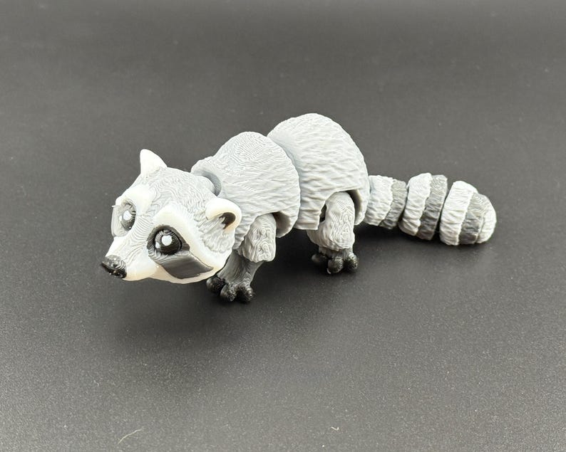 May include: A grey and white articulated raccoon toy with black eyes and a black nose. The toy is made of plastic and has a segmented tail.