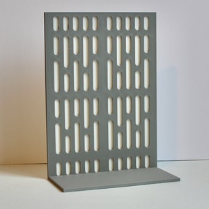 May include: A gray, rectangular display stand with a series of vertical and horizontal cut-out slots. The stand has a base for stability and a back panel with a repeating pattern of elongated openings. The background is white.
