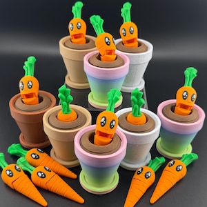 May include: A collection of nine small ceramic pots with cartoon carrot faces. Each pot is painted in a different color, including brown, pink, white, and green. The carrots are all orange and have green tops.