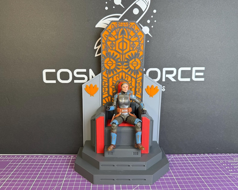 May include: A detailed action figure of a character seated on a throne. The throne is gray, orange, and red, with intricate geometric designs. The figure is wearing armor with blue and brown accents. The background features the text "COSMOS FORCE".