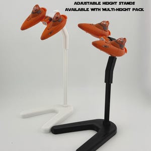 May include: Two orange toy spacecraft are displayed on white and black stands. The stands have a unique angled base. Text on the image reads: ANGLE STANDS AVAILABLE WITH DYNAMIC PACK. ADJUSTABLE HEIGHT STANDS AVAILABLE WITH MULTI-HEIGHT PACK.