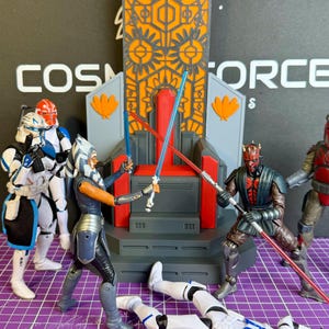 May include: Action figures of Star Wars characters in a battle scene. Ahsoka Tano and Darth Maul are engaged in a lightsaber duel, with other figures and a throne in the background. The word "Cosmoforce" is visible.