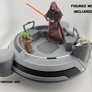 以下が含まれることがあります： 「FIGURES NOT INCLUDED」と「STANDARD SIZE」の文字が入った、グレーと黒のスターウォーズをテーマにしたプレイセット。 プレイセットは、座席エリアと中央のプラットフォームを備えた円形デザインです。 2つのアクションフィギュアがプレイセットに配置されています。