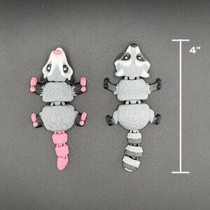 May include: Two small, grey and white, segmented, plastic animal figurines. One is a raccoon with a black tail and the other is a possum with a pink tail. Both are 10 cm tall.