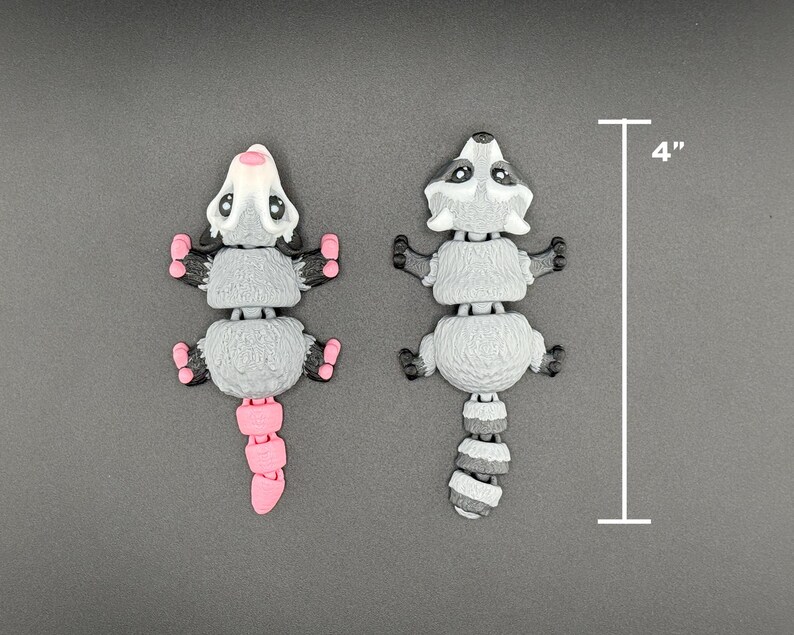 May include: Two small, grey and white, segmented, plastic animal figurines. One is a raccoon with a black tail and the other is a possum with a pink tail. Both are 10 cm tall.