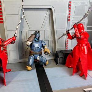 Puede incluir: Escena con figuras de acci&oacute;n en un entorno de ciencia ficci&oacute;n. Dos figuras con armadura roja se enfrentan a una figura con armadura azul. Una figura roja empu&ntilde;a una espada, la otra una lanza. La figura azul est&aacute; arrodillada, aparentemente angustiada.