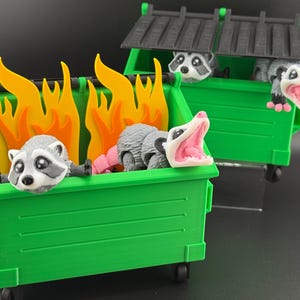 May include: Three raccoons are sitting in green wheelie bins. One wheelie bin has flames coming out of the top. The raccoons are all looking at the camera.