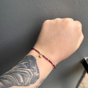 May include: A delicate bracelet made of small, dark red beads with a gold heart charm.
