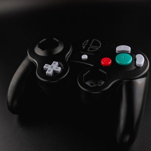 May include: Black video game controller with a gray directional pad, gray, red, green, and white buttons. The controller has a logo on the top and two handles. The controller is designed for gaming.