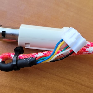 以下が含まれることがあります： 赤と白の編組ケーブルが付いた白と銀のビデオゲームコントローラーコネクタ。コネクタは、6本のワイヤーが付いた白いプラスチックコネクタです。