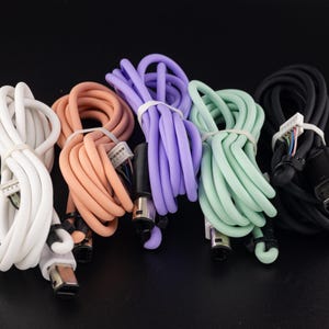 May include: A set of six colorful cables with different connectors. The cables are coiled and arranged in a semi-circle. The cables are white, light pink, purple, light green, black, and dark gray.
