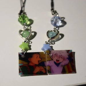 May include: Two phone charms featuring square acrylic pendants with anime characters. The left charm has a green faceted bead, a heart charm with a light green bead, and a lime star. The right charm has a clear bead, a heart charm with a light blue bead, and a periwinkle star.