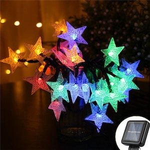 May include: A string of solar powered fairy lights with star-shaped bulbs in various colors, including red, orange, yellow, green, blue, and purple. The lights are strung around a clear glass vase and are powered by a small solar panel.