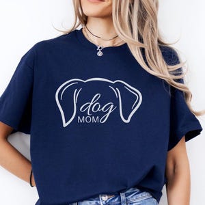 T-Shirt featuring a minimalist design with dog ears and the phrase 'dog MOM' in cursive, perfect for dog lovers who want to showcase their love for their pets in a stylish and comfortable way.