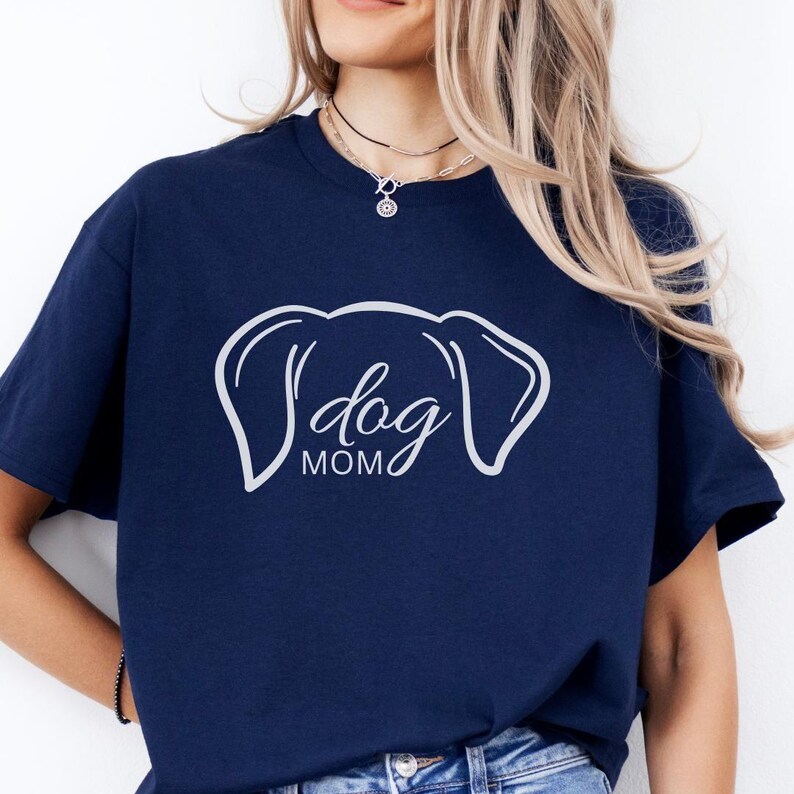 T-Shirt featuring a minimalist design with dog ears and the phrase 'dog MOM' in cursive, perfect for dog lovers who want to showcase their love for their pets in a stylish and comfortable way.