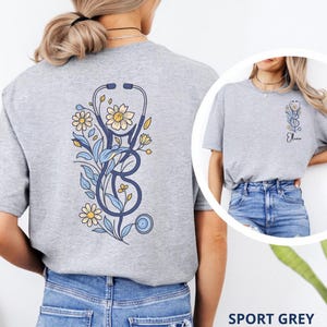May include: A t-shirt with a blue stethoscope and floral design on the back. The front of the sweatshirt has a smaller blue stethoscope and floral design with the name 'Olivia' printed below it.