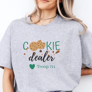 Cookie dealer sweatshirt featuring playful cookie graphics and troop number text. Cozy neutral crewneck styled casually, perfect for Girl Scout cookie season, troop events, and booth days.