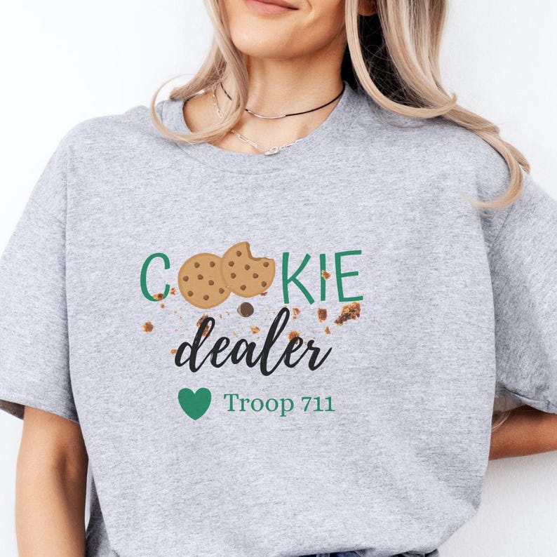 Cookie dealer sweatshirt featuring playful cookie graphics and troop number text. Cozy neutral crewneck styled casually, perfect for Girl Scout cookie season, troop events, and booth days.