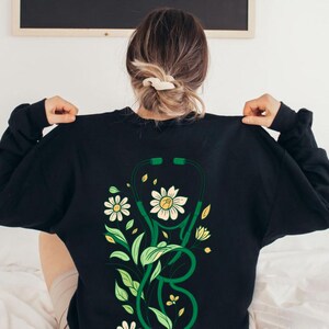 May include: A sweatshirt with a green stethoscope and floral design on the back.